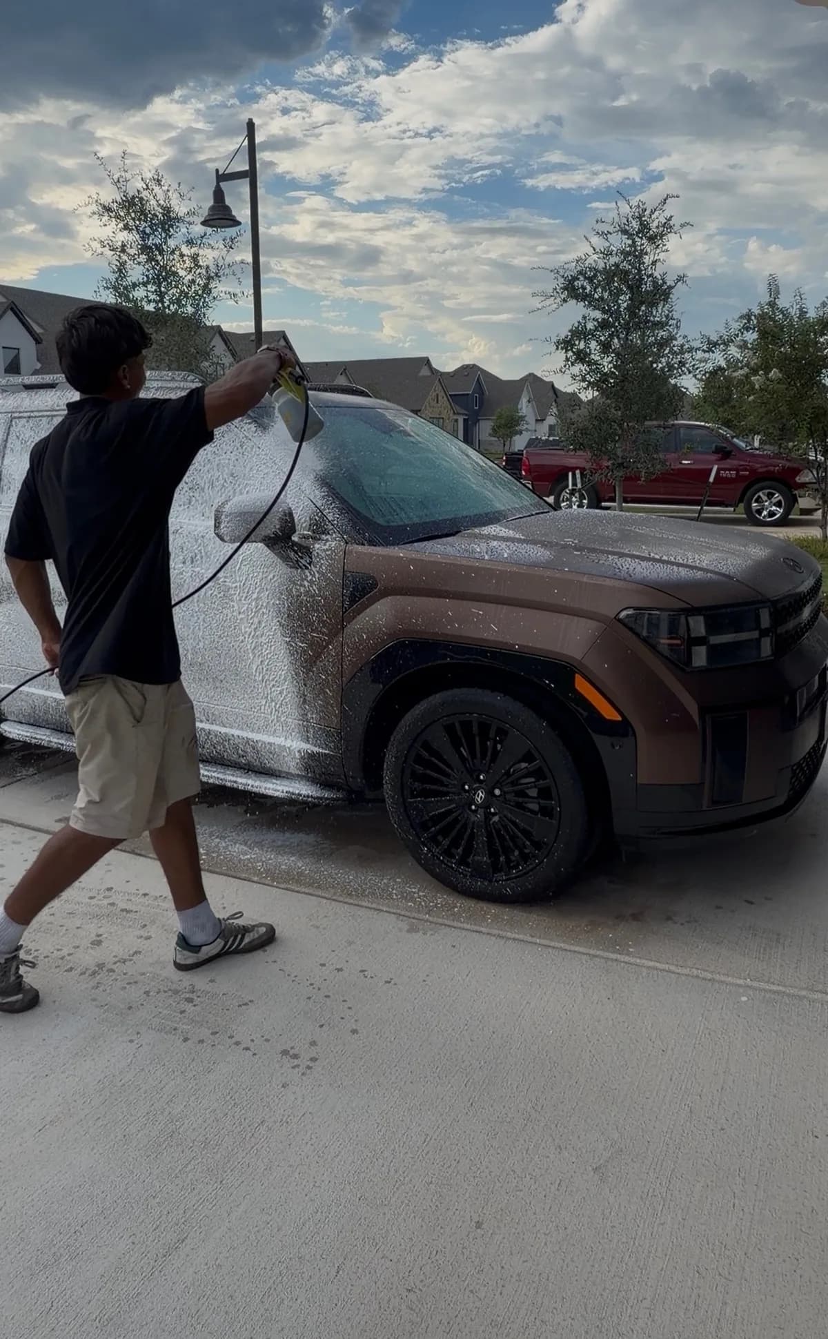 The owner of We Detail Austin applying foam to a bronze Hyundai SUV in a driveway